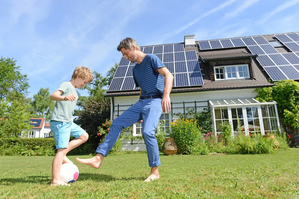 Einfamilienhaus mit PV_Vater und Sohn spielen im Vordergrund im Garten Fußball