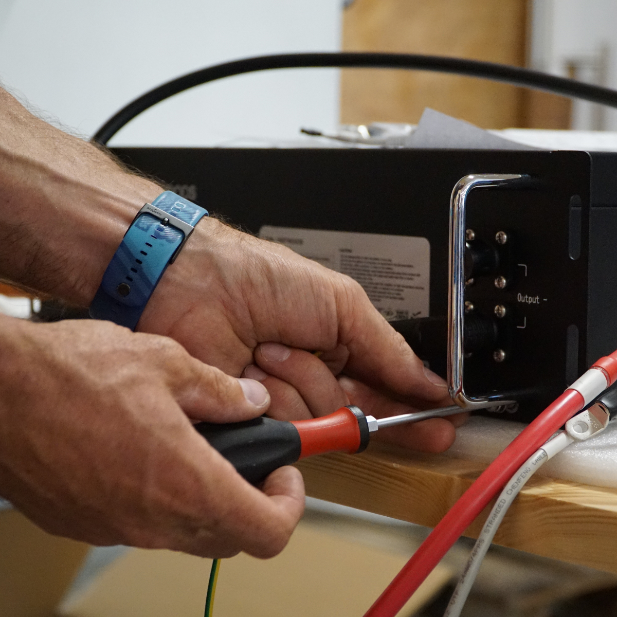 Fachmännische Montage des YOULIQ one: Ein Techniker schließt mit einem Schraubendreher die Verkabelung an das Batteriemodul des Stromspeichers an.